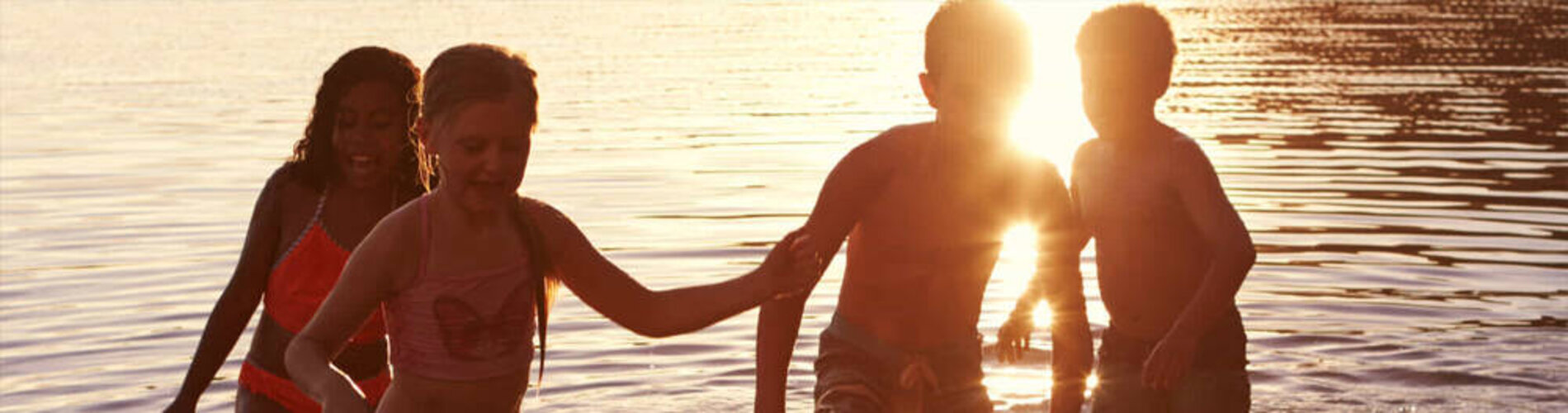 Four children exiting the lake at sunset.